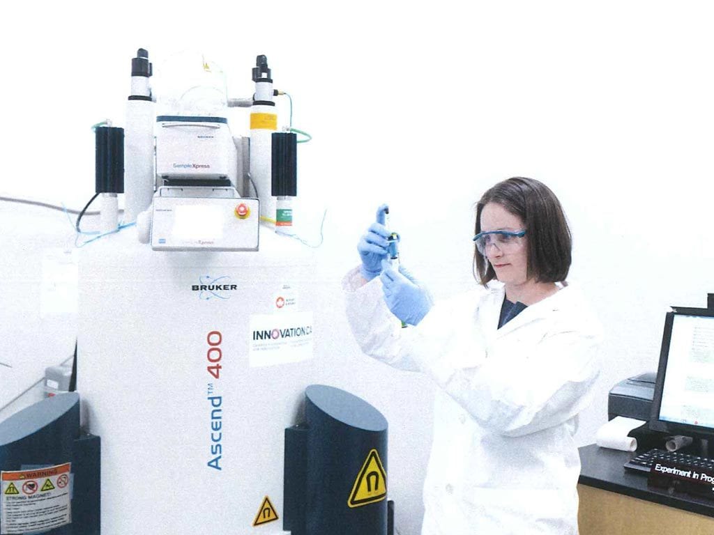 Female scientist beside Nuclear Magnetic Resonance spectrometer.