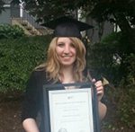 Female graduate in cap and gown holding framed diploma.