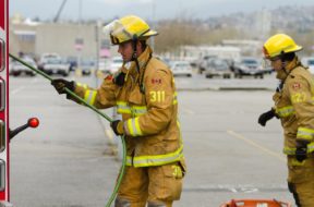 Two firemen dressed in yellow suits work with equipment.