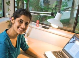 Woman with brown hair seated with laptop in front smiling.