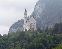 view of Neuschwantein Castle with trees and mountains surrounding it.