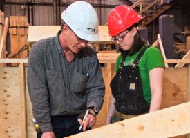 Man and woman with safety hats in a carpentry workshop.