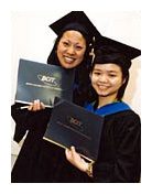 Two students wearing black graduation caps and gowns holding black diplomas.