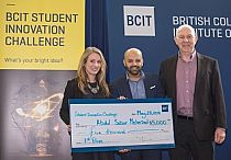 Photo of two students holding a cheque and another person standing beside them.