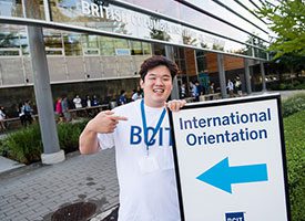 Student holding a sign saying international orientation in dark blue text and a light blue arrow underneath the text.