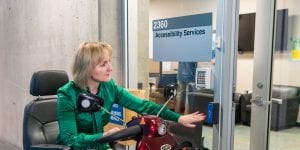 Woman in mobility scooter press the open door button to enter the accessibility services office.