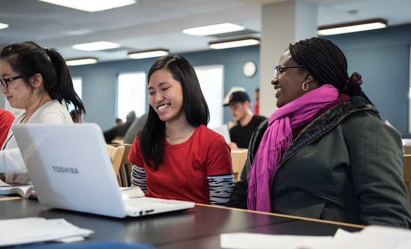 Female students smiling and looking at a laptop.