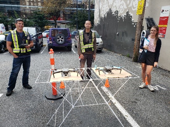 Two men and one woman standing behind a table with two drones