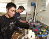 two male students in navy t-shirts look at some mechanical pieces
