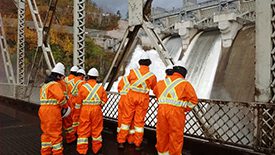 eight men in orange jumpsuits looking at a dam