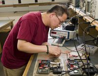 man in burgundy t-shirt with glasses looking at an electrical board