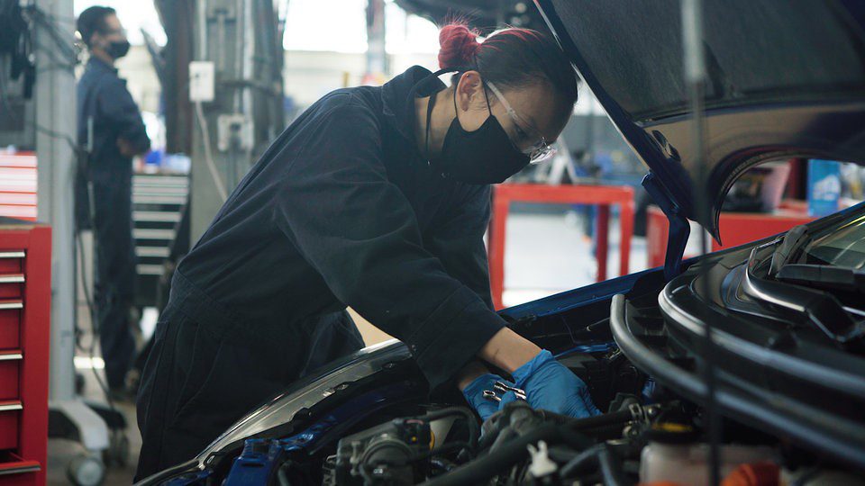 BCIT student wearing mask working under the hood of a car