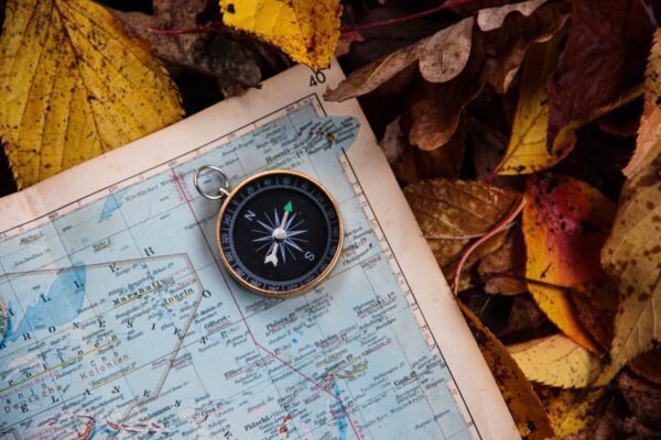 Compass and map on autumn leaves.