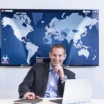 Derek Manky in a boardroom wearing a suit with the Fortinet logo behind him