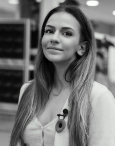 black and white photo of a female with long blonde hair, a lapel mic, wearing a white v neck long sleeve top