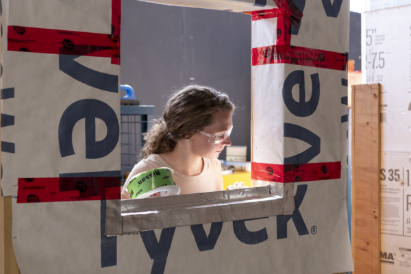 Student standing behind a wall inspecting the airtight tapes used to seal the window opening