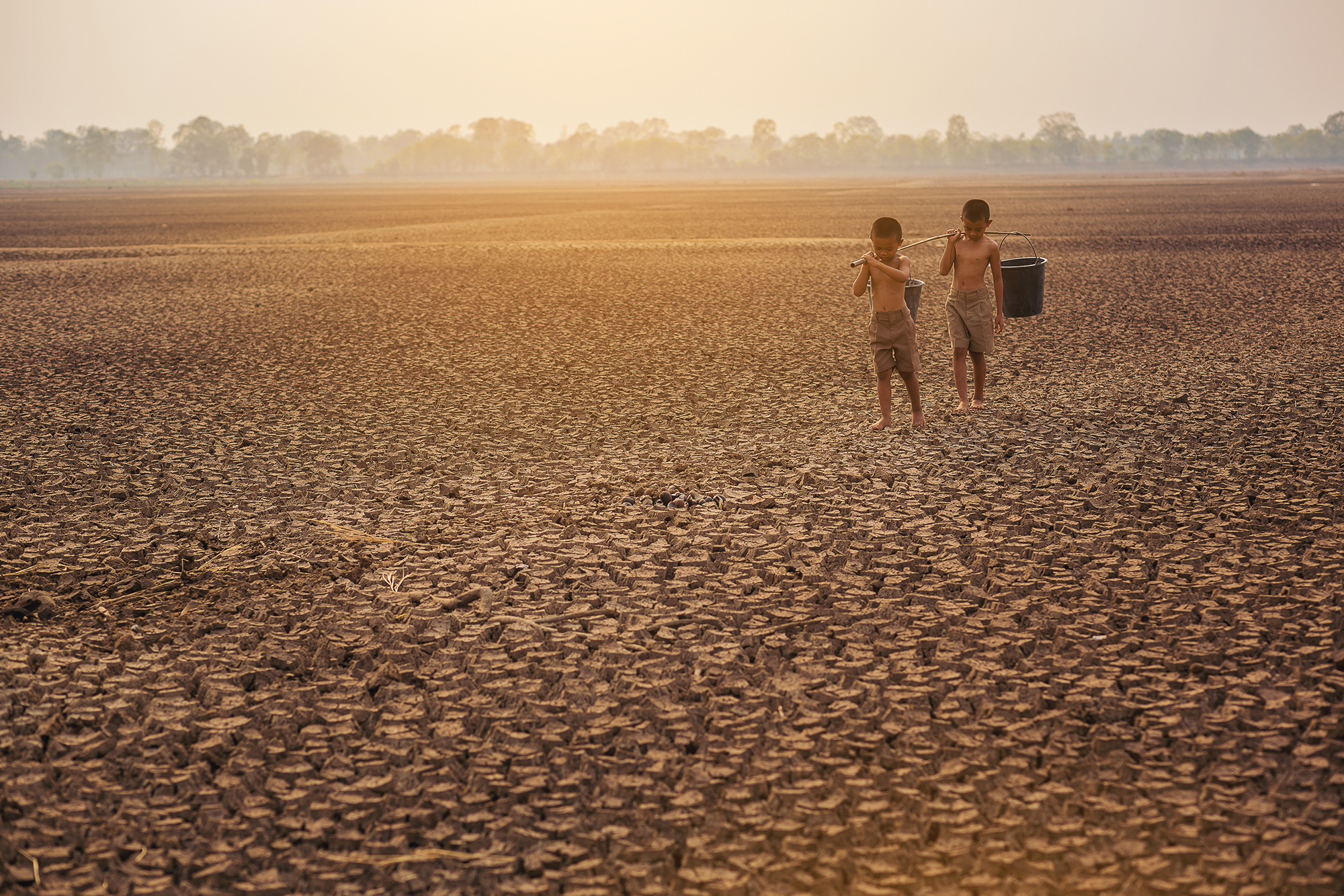 Asian local boys at large dry cracked landscape looking for water.