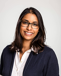 Hazrah Moothoo with brown shoulder length hair, black glasses, white dress shirt, and a black cardigan 