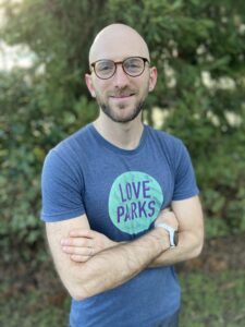 Nathan, bald with beard wearing black glasses and a blue shirt that says love parks