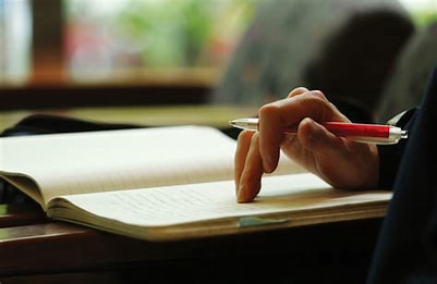 Person holding a red pen to write on a noteboo